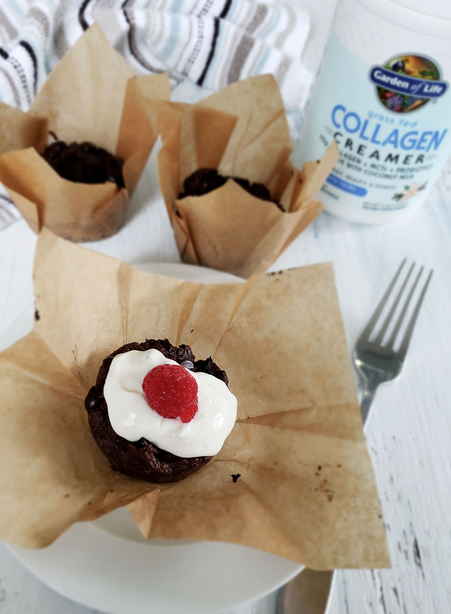 double chocolate chip cupcakes with Garden of Life Grass Fed Collagen and Greek Yogurt topping garnished with a red raspberry.