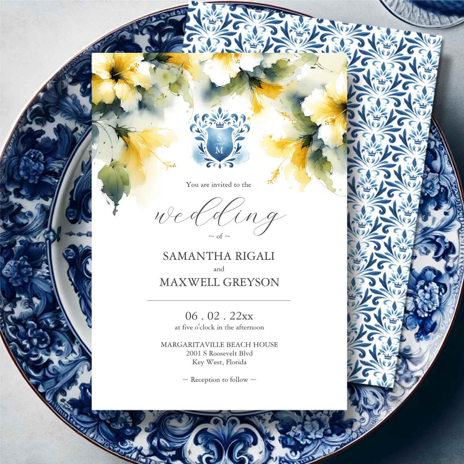 Wedding invitations feature watercolor blue monogrammed crest and yellow hibiscus flowers. 