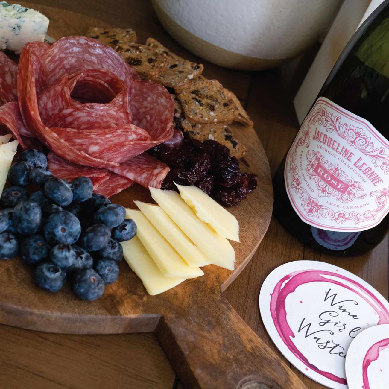 Charcuterie board with gourmet meats, cheeses, and fruit served alongside a chilled bottle of sparkling rosé, styled as part of wine bridal shower theme food ideas for an elegant celebration.