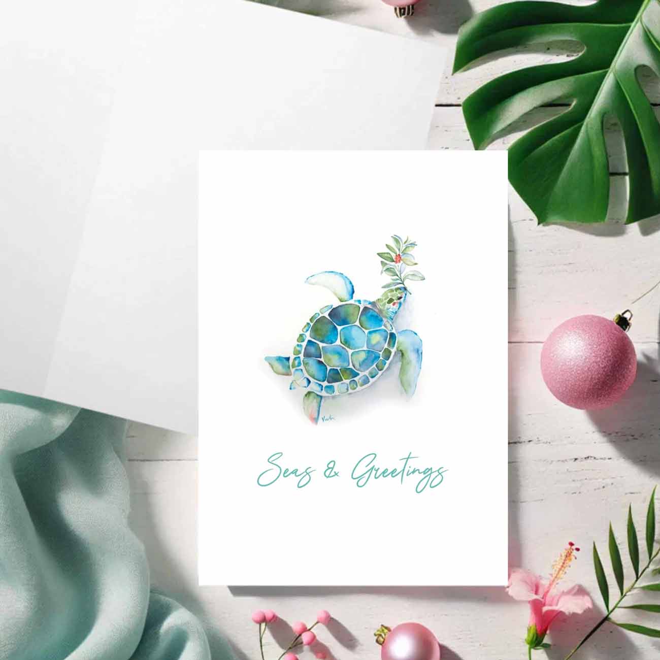 Flat lay of a beach Christmas card with a watercolor sea turtle by Victoria Grigaliunas of Do Tell A Belle. The words Seas & Greetings are set in trendy blue script typography. Tap to shop our small business store online.
