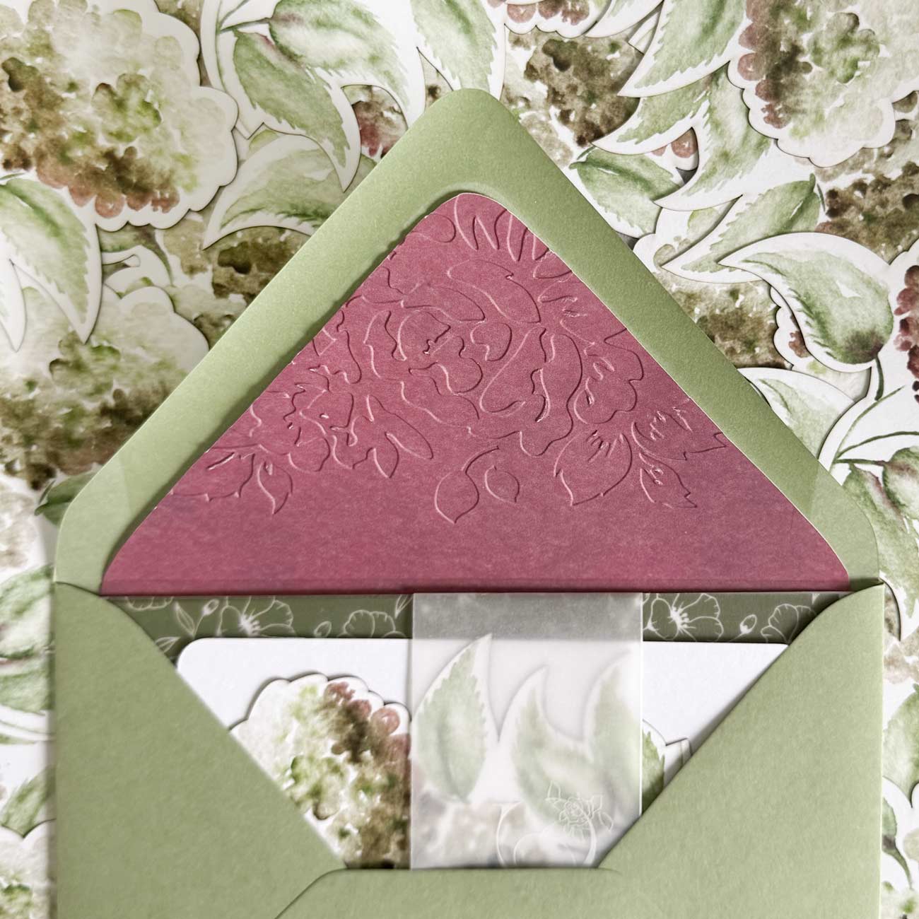 Handcrafted embossed envelope liners in burgundy floral embossing paired with olive green envelopes and luxury wedding stationery suite details.
