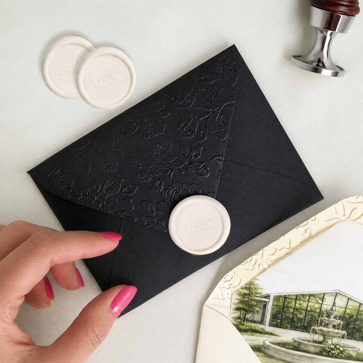 Custom ivory wax seal on wedding invitations featuring a personalized monogram, displayed on a black embossed envelope with luxury wedding stationery details.