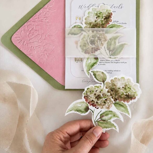 Watercolor die cut wedding invitations featuring olive green envelopes, a pink embossed envelope liner, vellum monogram belly band, and a die cut hydrangea RSVP card in a custom wedding stationery suite.