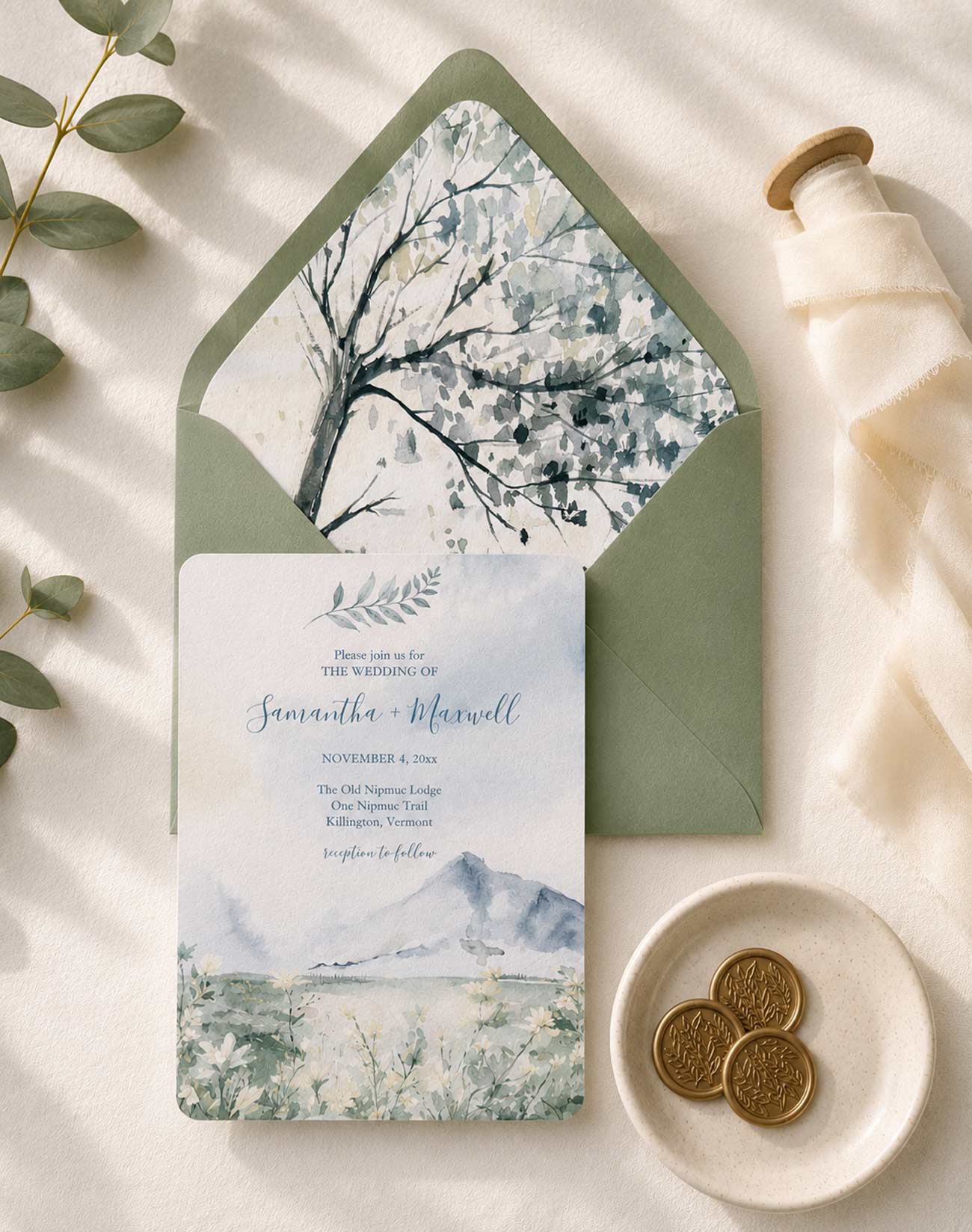 Watercolor mountain wedding invitations in dusty blue and sage green featuring a hand-painted mountain landscape invitation, watercolor tree envelope liner, and coordinating wedding stationery suite.
