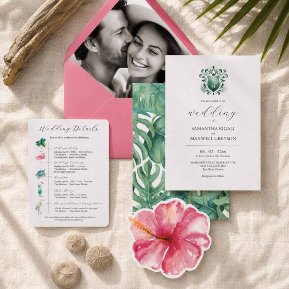 Destination wedding invitation suite featuring tropical watercolor monstera leaves, a pink envelope with black-and-white engagement photos, a custom wedding invitation, timeline details card, hibiscus die-cut embellishment, and coordinating beach-inspired wedding stationery arranged in a styled flat lay.
