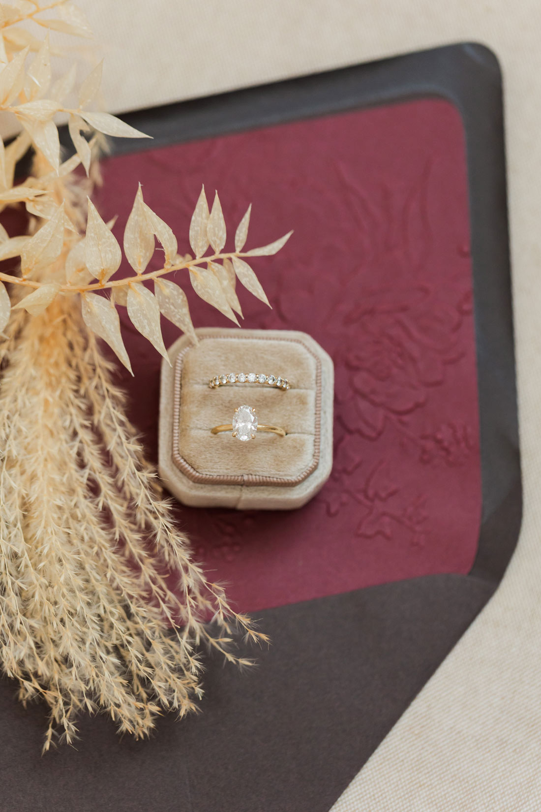 Burgundy embossed floral envelope liner with chocolate brown envelope, styled with wedding rings and dried florals.