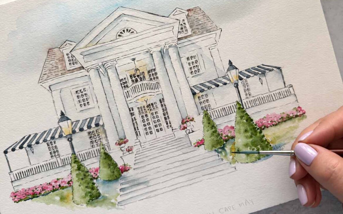 Watercolor wedding venue artist Victoria Grigaliunas hand-painting an architectural illustration of Peter Shields Inn in Cape May, featuring elegant columns, pink flowers, and lush greenery.